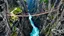 Placeholder: In a fantasy world, a deep gorge with vertical stone sides has a tumultuous river flowing at the bottom. At ground level, above the gorge, a rope bridge has been constructed to span across the gorge. People are walking across the bridge. The scenery is awe-inspiring. Colour photograph.