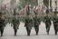 Placeholder: Soldiers marching in formation; military parade; marching along a street; green uniforms; medals and insignia; Rifles in their hands;