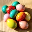Placeholder: An 8k resolution, 16:9 aspect ratio photograph, photorealistic style, capturing a meticulously arranged cluster of Easter eggs on a rustic light oak surface. The eggs, flawlessly smooth and glossy, reflect soft, diffused natural light, showcasing a vibrant palette of azure, emerald, ruby, golden yellow, and blush pink. Intricate patterns—delicate floral motifs and abstract swirls—are subtly visible on each egg, some accented with flecks of gold leaf. The eggs cast subtle, soft shadows, highlig