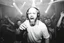 Placeholder: en manlig skallig och goatee (ansat skägg) DJ (med hörlurar) som sjunger nära in i kameran, väldigt exalterad, och folk som dansar våldsamt i backgrunden på ett techno disco, svartvit bild, prodigy trash style