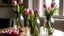 Placeholder: A closeup of long-stemmed pink tulips with glass jars on a round table.
