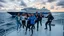 Placeholder: a group of young ladies and young men in sports pants and jacket are dancing to camera on deck of a small modern ship in oceion next to a passing huge ship,cloudy sun set sky