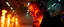 Placeholder: close up portrait of a plasma vampire flickers like hypnotic fire A cavernous industrial warehouse becomes a fever-dream carnival of fire and smoke, lit exclusively by erratic strobes and the orange glow of unpredictable blazes. The world is drenched in soot, haze, and manic energy — walls drip with condensation, fire extinguishers become absurd props, and every surface reflects the flicker of flames being born and killed in seconds. The visual journey spirals from controlled chaos to full unhin