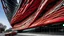 Placeholder: Architectural photograph of the Petersen Automotive Museum in Los Angeles, California, featuring a design of stainless steel ribbons over a red facade, under a gray sky. The ribbons are arranged in a wave-like pattern, creating a dynamic and fluid appearance. The red facade is visible between the ribbons, providing a contrasting color that accentuates the building's unique design. The sky is overcast, which creates a soft, diffused light that highlights the building's texture and form. The photo