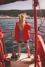 Placeholder: 23 years old girl, with blond hair and a messy bun. standing on in a red boat, wearing red clothes and looking trough binoculars watching something in the middle of the sea. You see the whole boat