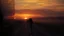 Placeholder: A modern cinematic video about heartbreak and separation. A lone person stands on an empty road at sunset while a train or caravan disappears into the distance. The scene is emotionally powerful, realistic, and visually elegant. Show modern symbolic imagery: reflections in glass, a phone screen lighting up with an unanswered message, a floating dust cloud, a broken mirror, and a silhouette walking away through soft fog. Use dramatic camera movement, shallow depth of field, emotional close-ups,